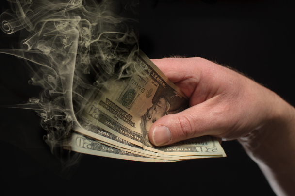 A hand holds money that is burning away.