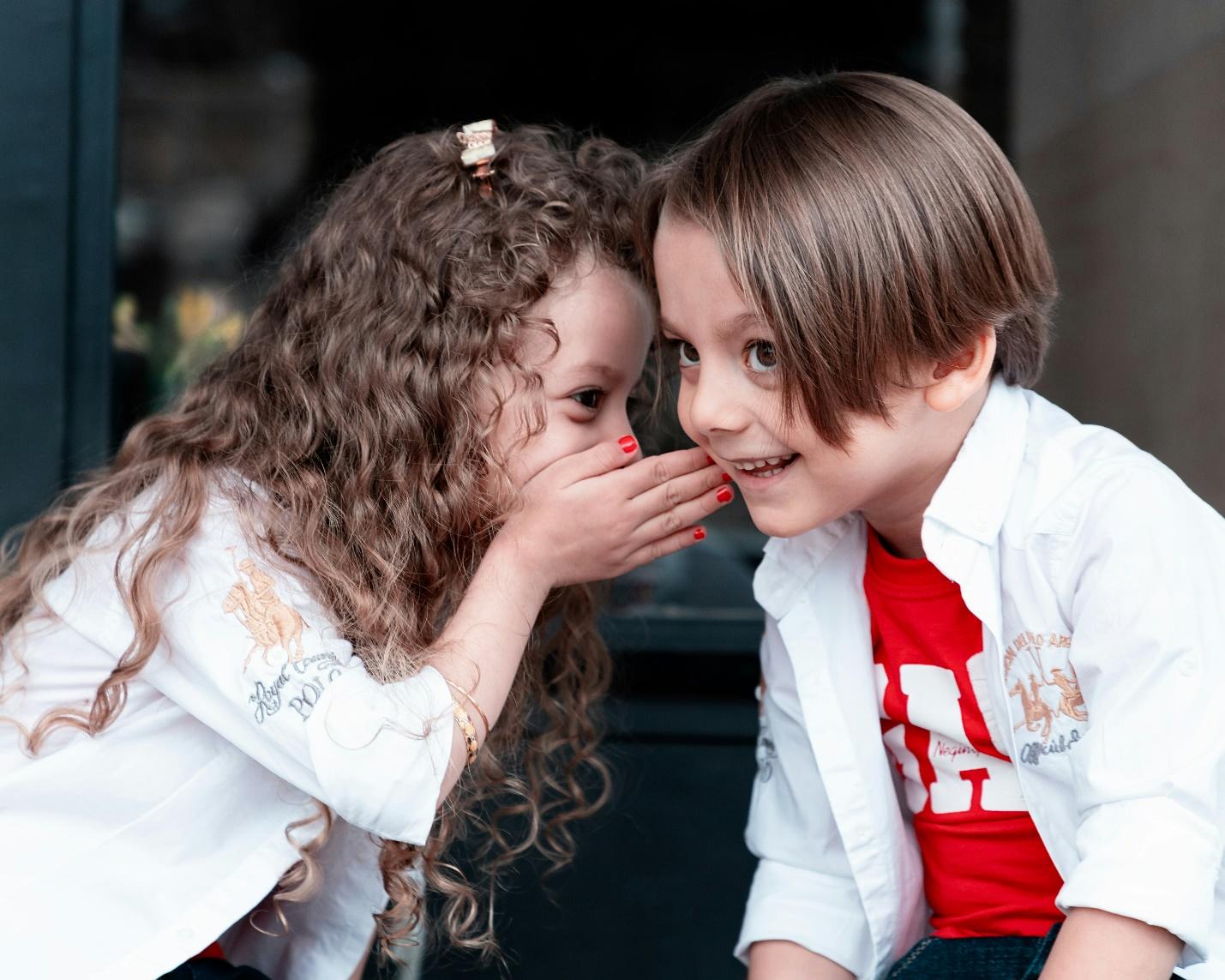 A child whispering to a childDescription automatically generated